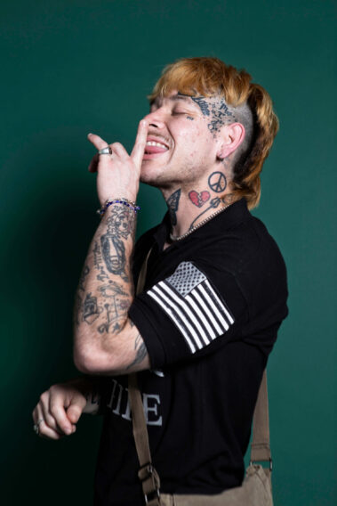 Tattooed attendee posing playfully against a green backdrop during the MAYHEM event.