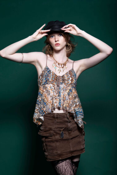 Model wearing a patterned outfit and black hat posing against a green backdrop during MAYHEM.