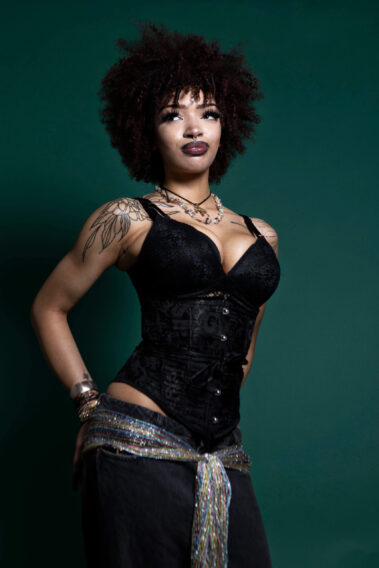 Model in black corset-style fashion posing confidently against a green backdrop during the MAYHEM event.