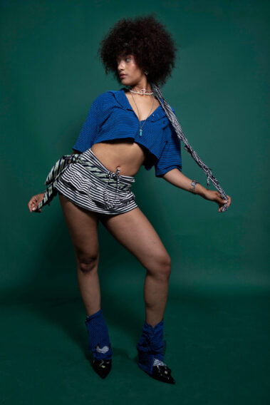 Model posing in a blue outfit with bold fashion styling against a green studio backdrop during the MAYHEM event in Oklahoma City.