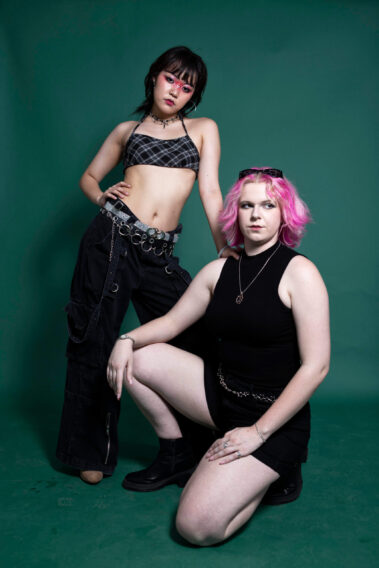 Two alternative fashion models posing together against a green backdrop during the MAYHEM event.