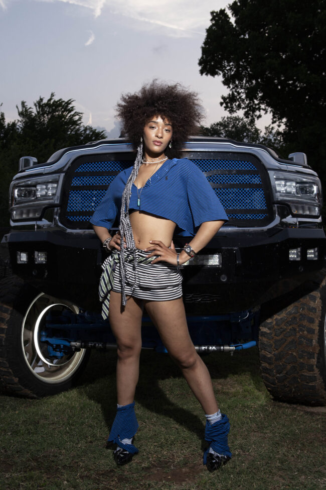 Model posing in front of a lifted black truck outdoors during the MAYHEM event photoshoot.
