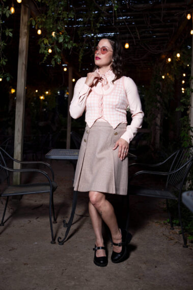 Portrait of Gema Khaos posing beneath hanging string lights at Castle Falls during a 1940s-themed photomeet, wearing a pastel vintage-inspired outfit and round pink glasses.