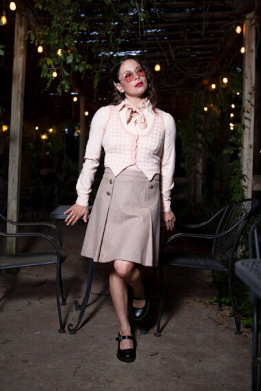 Gema Khaos posing in a vintage-inspired outfit between outdoor café tables beneath glowing lights at Castle Falls during a themed photography event.