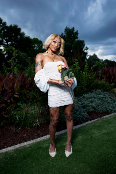 nq.liyahh holding roses while posing in a white dress beneath dramatic storm clouds at Will Rogers Gardens during the Garden Party photoshoot.
