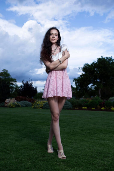 caitlinrmathews standing on a grassy lawn in a pink lace dress during an outdoor Garden Party portrait session at Will Rogers Gardens.