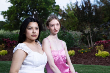 Alise_Rojo in a white dress and Mariah_Rain_ in a pink satin dress posing together in a landscaped garden during an outdoor portrait session.