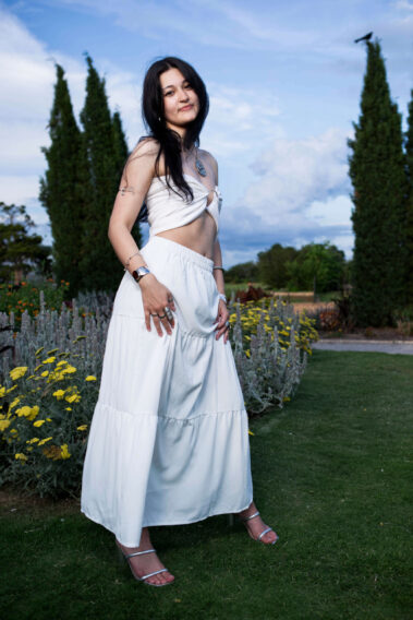 Bella Bazan posing in a flowing white outfit beside blooming flowers at Will Rogers Gardens during the Garden Party photoshoot.
