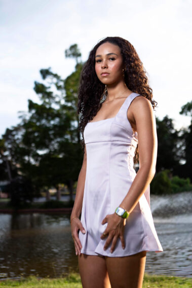 TielaFaith posing beside a pond in a light lavender satin dress during a golden hour portrait session at a garden park.