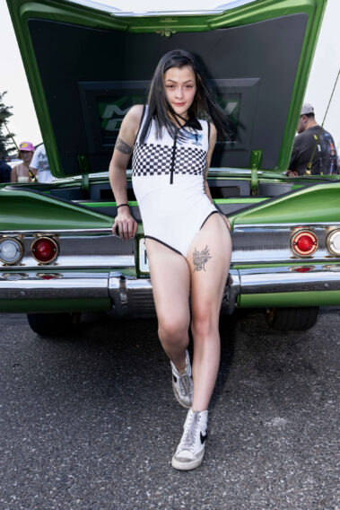 Ice Angels model standing in front of a customized green classic car with the trunk open.