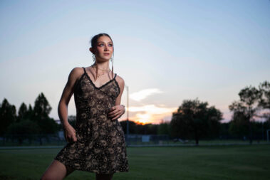 Portrait of a model with alternative fashion styling, dark dress, and colorful makeup standing in a wooded park.