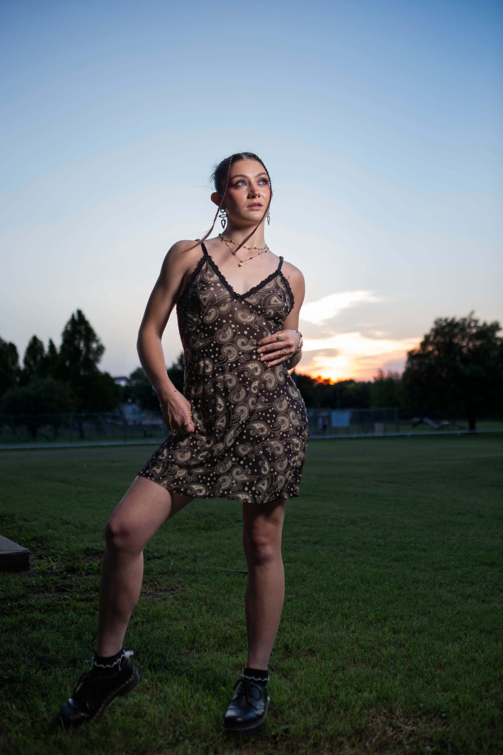 Twilight Reverie Portrait of a model wearing a patterned slip dress posing in a grassy field at sunset with a colorful evening sky in the background.