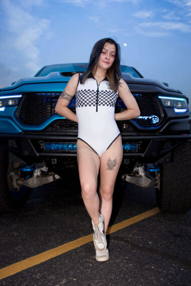 Ice Angels model standing in front of a customized Ram TRX truck illuminated with blue accent lighting.