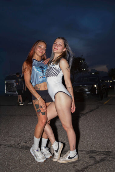 Two Ice Angels models pose together in a parking lot at dusk during the Street Motion car show as storm clouds gather overhead.