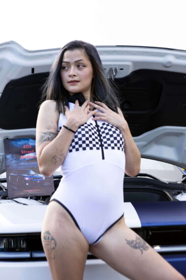 Ice Angels model posing in front of an open vehicle hood while wearing a racing-inspired outfit.
